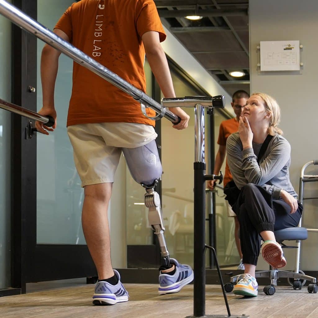 Limb Lab clinician, Erin, helping client as he walks on his prosthesis for the first time.