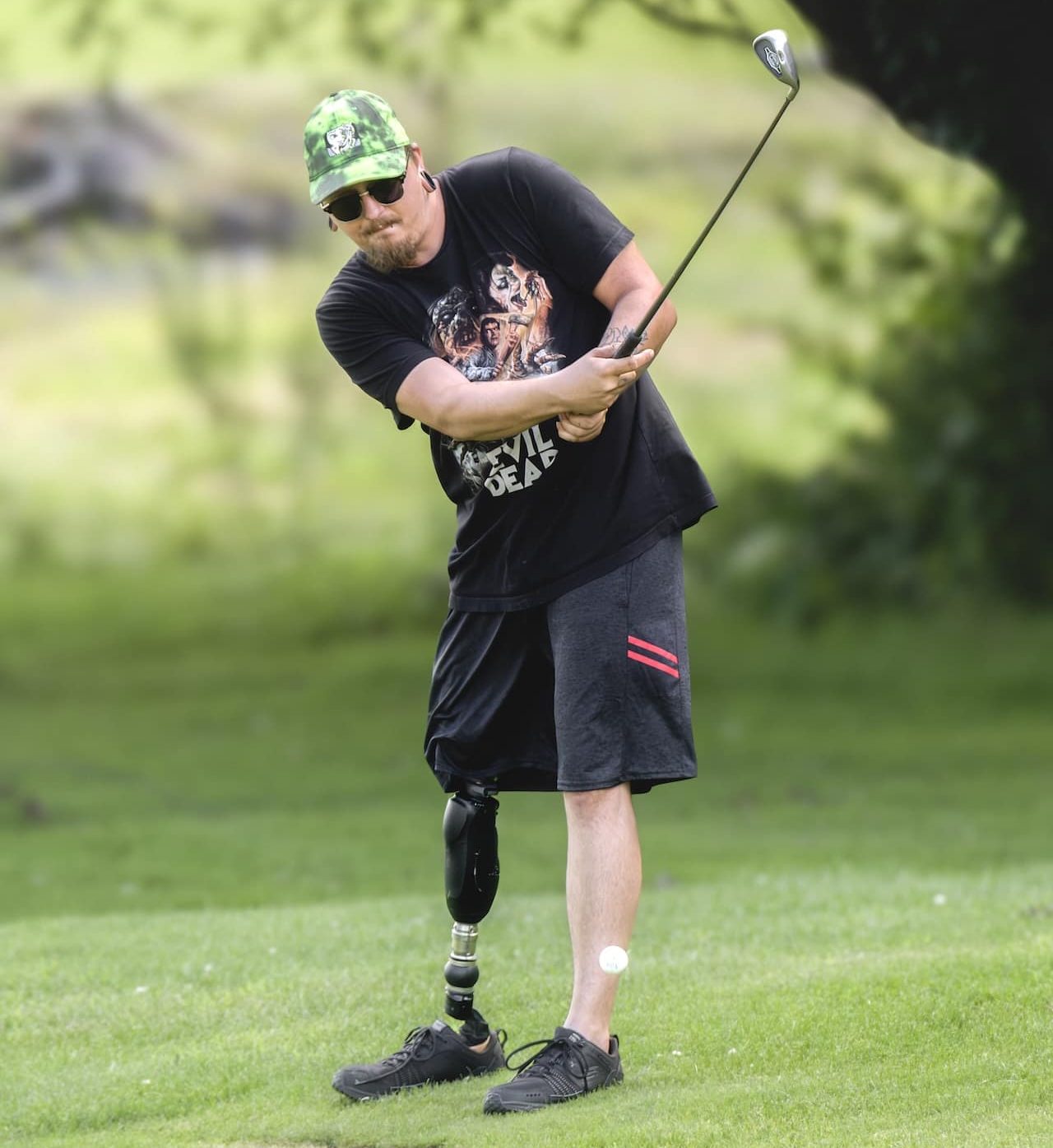 Man with a prosthetic leg swinging a golf club on a sunny golf course.