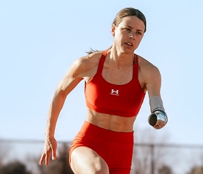 Female athlete with prosthetic arm sprinting in red sportswear on a track.