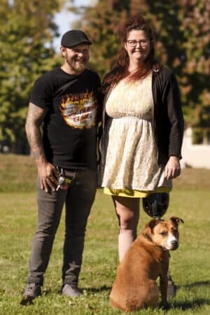 Couple smiling with a dog in a sunny park background