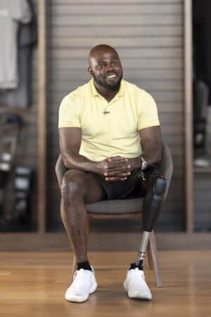Man in yellow shirt smiling while seated with a prosthetic leg in a casual setting