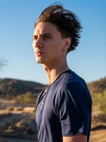 Man in blue shirt standing outdoors with a thoughtful expression in a desert landscape background