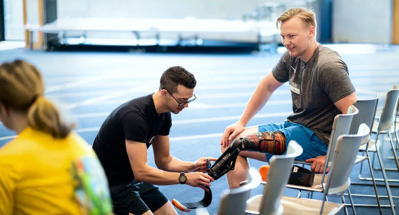 Trainer adjusts prosthetic leg on athlete in athletic facility.