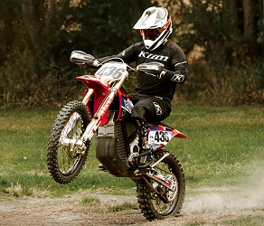 Motorcyclist performing a wheelie on a dirt bike in outdoor setting