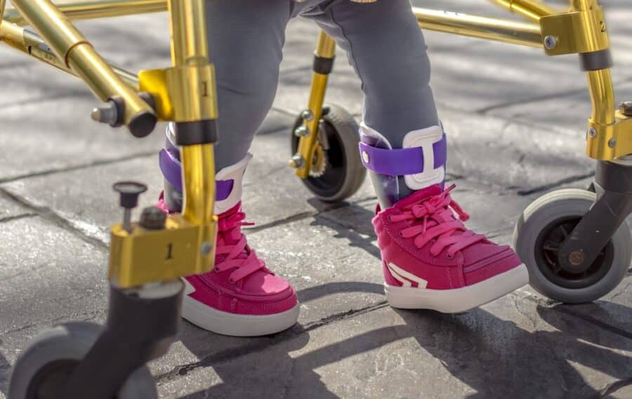 Child in bright pink sneakers using a walker outside on a sunny day.