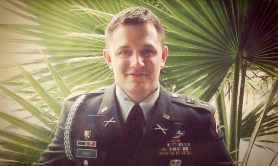 Soldier in formal uniform standing in front of palm leaves