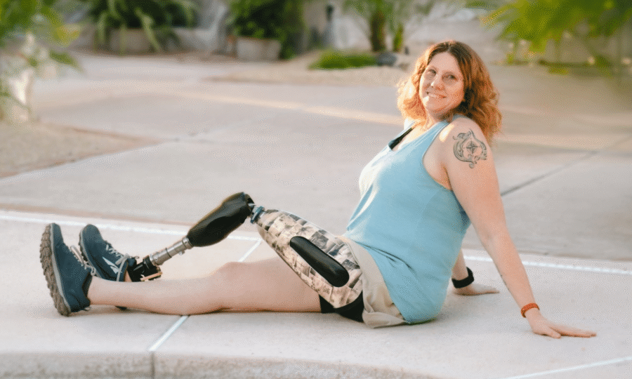 Woman with prosthetic leg sitting on pavement smiling outdoors