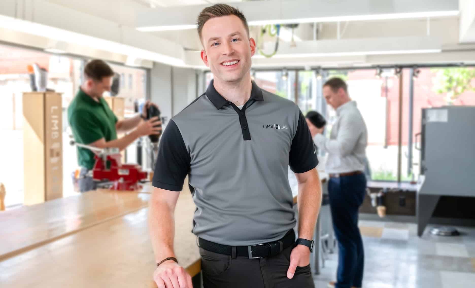 Man in a professional workspace wearing a gray Limb Lab shirt, with colleagues in the background