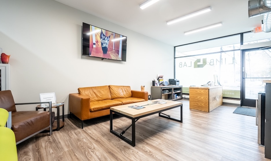 Modern waiting room with brown sofa, wooden tables, and large window providing natural light